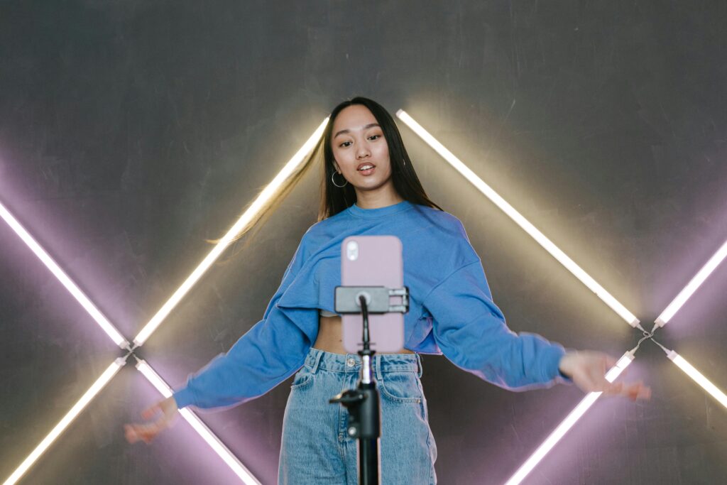 Teen influencer dances stylishly indoors, creating content using smartphone and ring light.